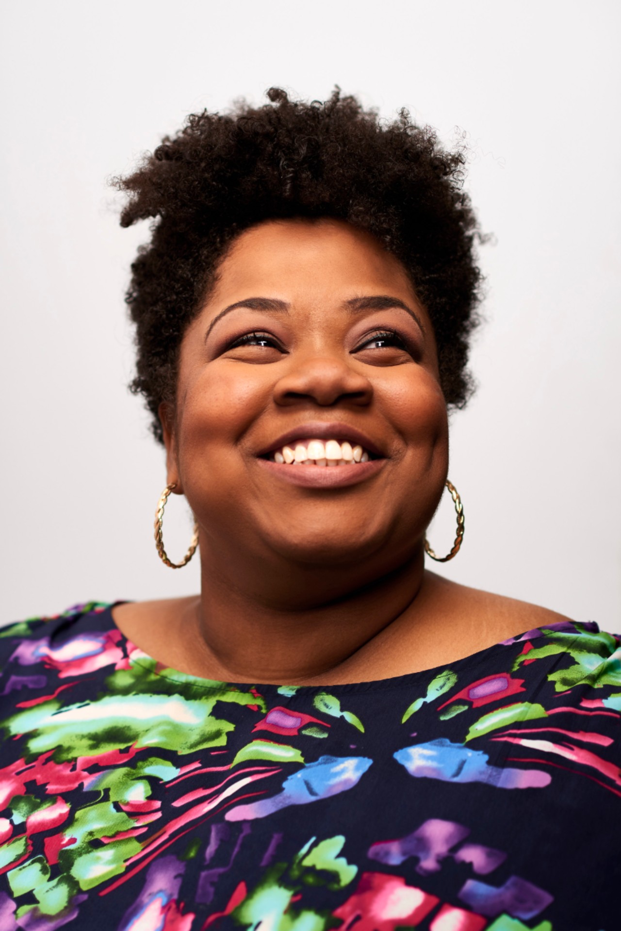 Headshot of a woman with hoop earrings and brightly colored blouse. Headshot of a woman with hoop earrings and brightly colored blouse.