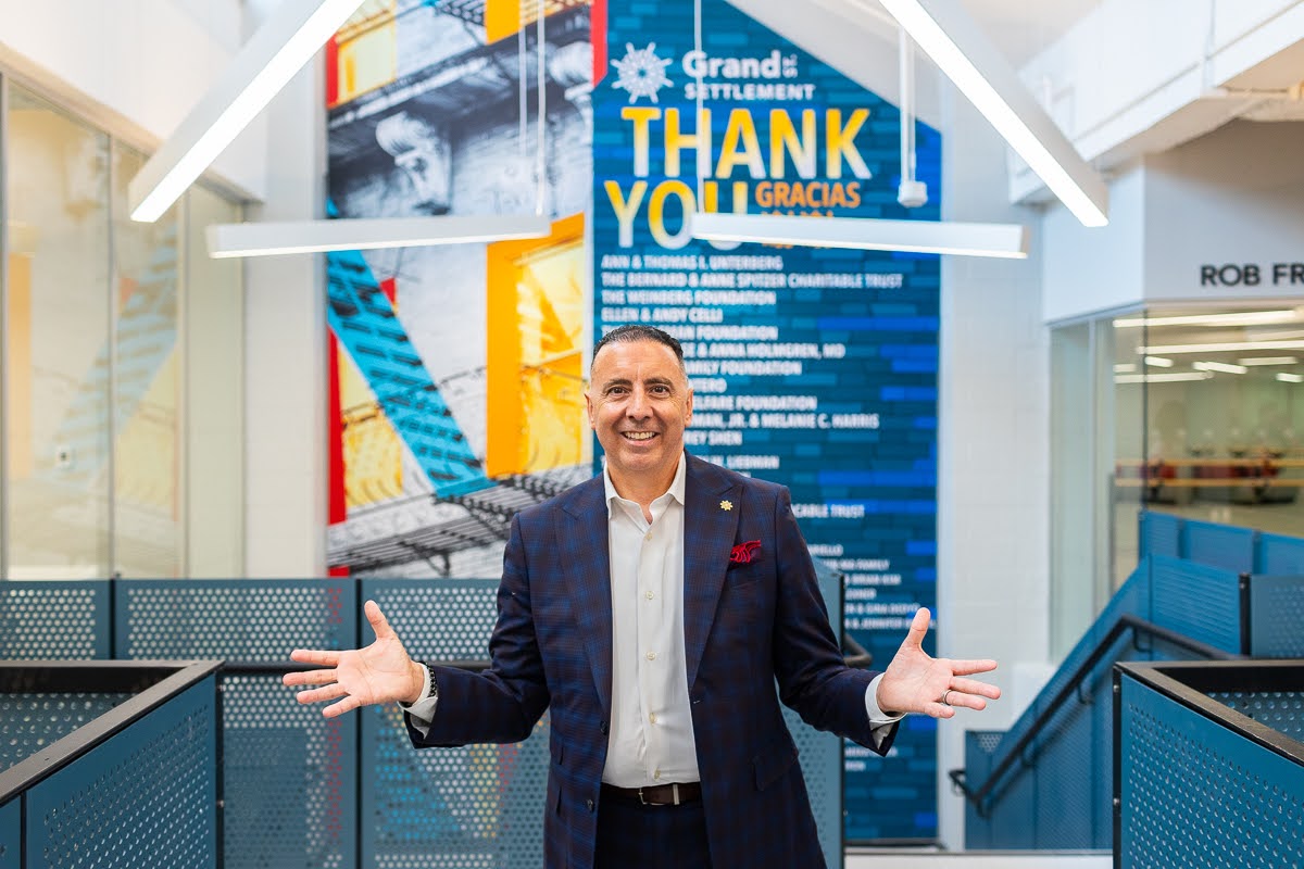 Grand St. Settlement CEO Robert Cordero celebrates the completion of their renovation in front of Grand Street's donor appreciation wall.