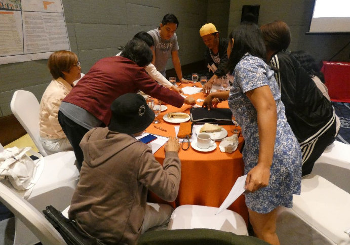 Workshop participants gathered around a table gesture to a document they're working on in the center.