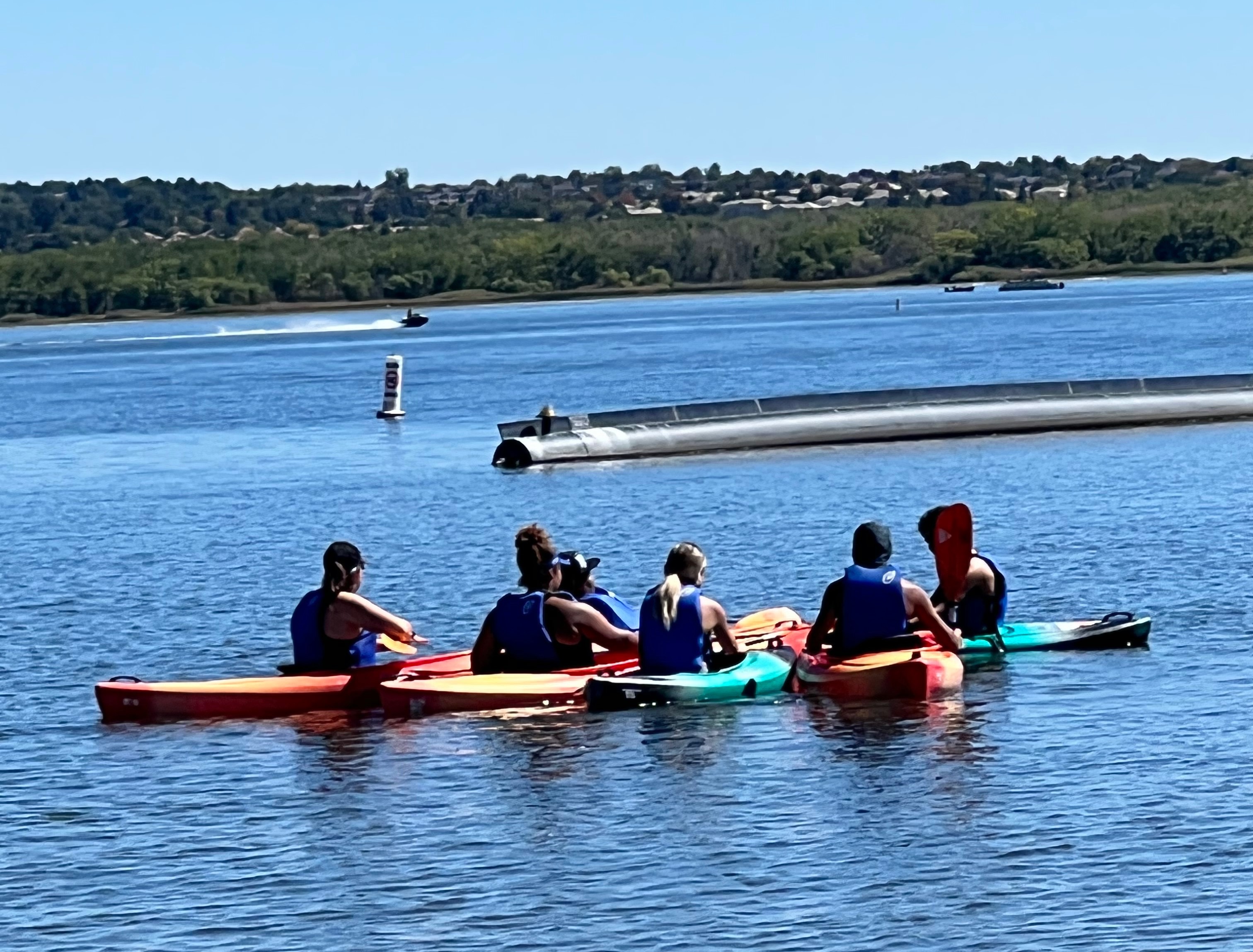 Several young people sit in two kayaks in the middle of a crystal blue lake. Several young people sit in two kayaks in the middle of a crystal blue lake.
