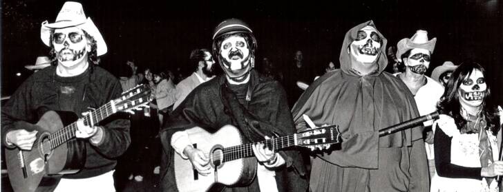 A black and white photograph of a group singing and playing guitar while wearing face paint. A black and white photograph of a group singing and playing guitar while wearing face paint.