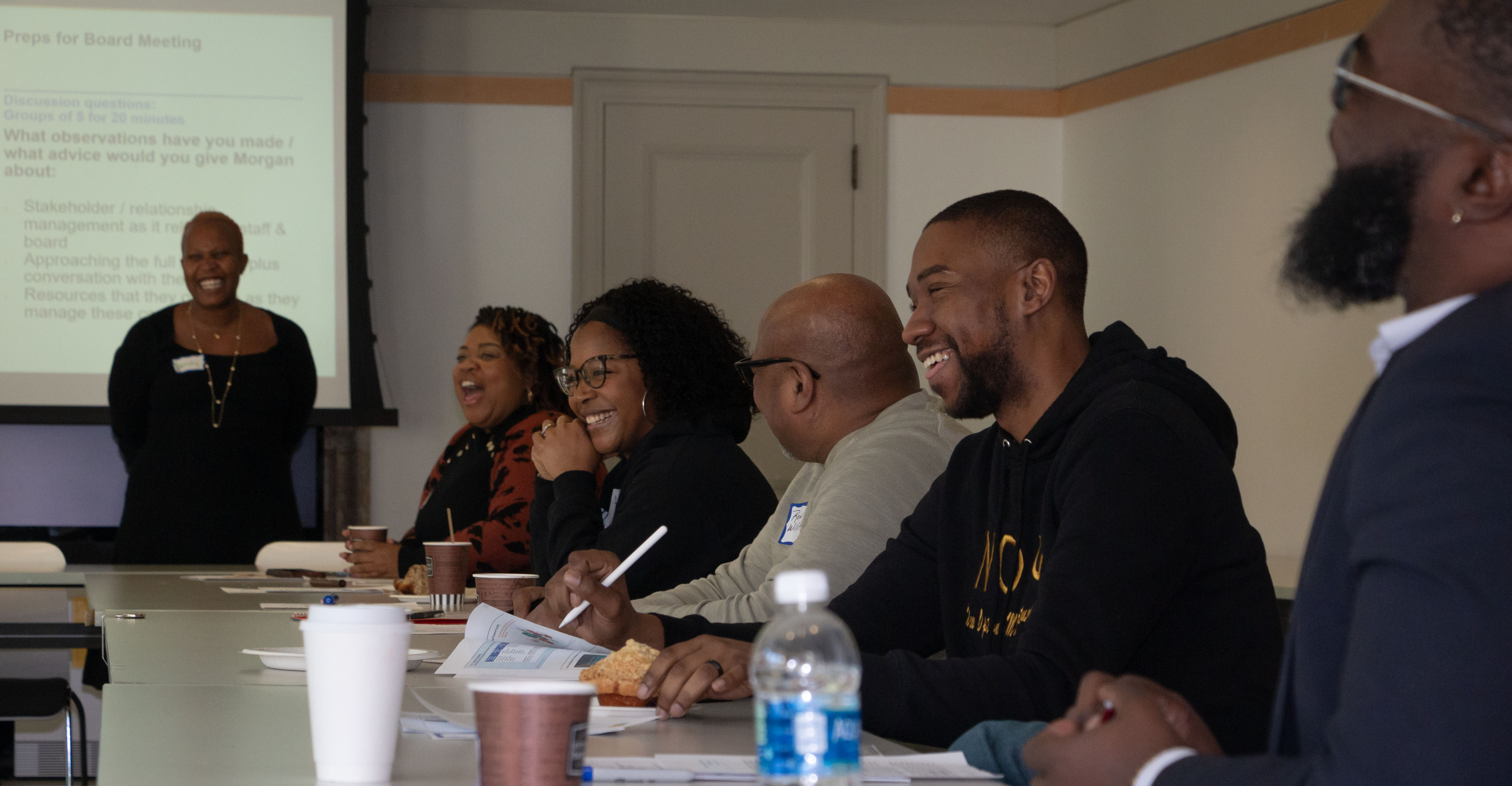 A row of BNCEP convening attendees seated at a table, with papers and pens out, laughing.