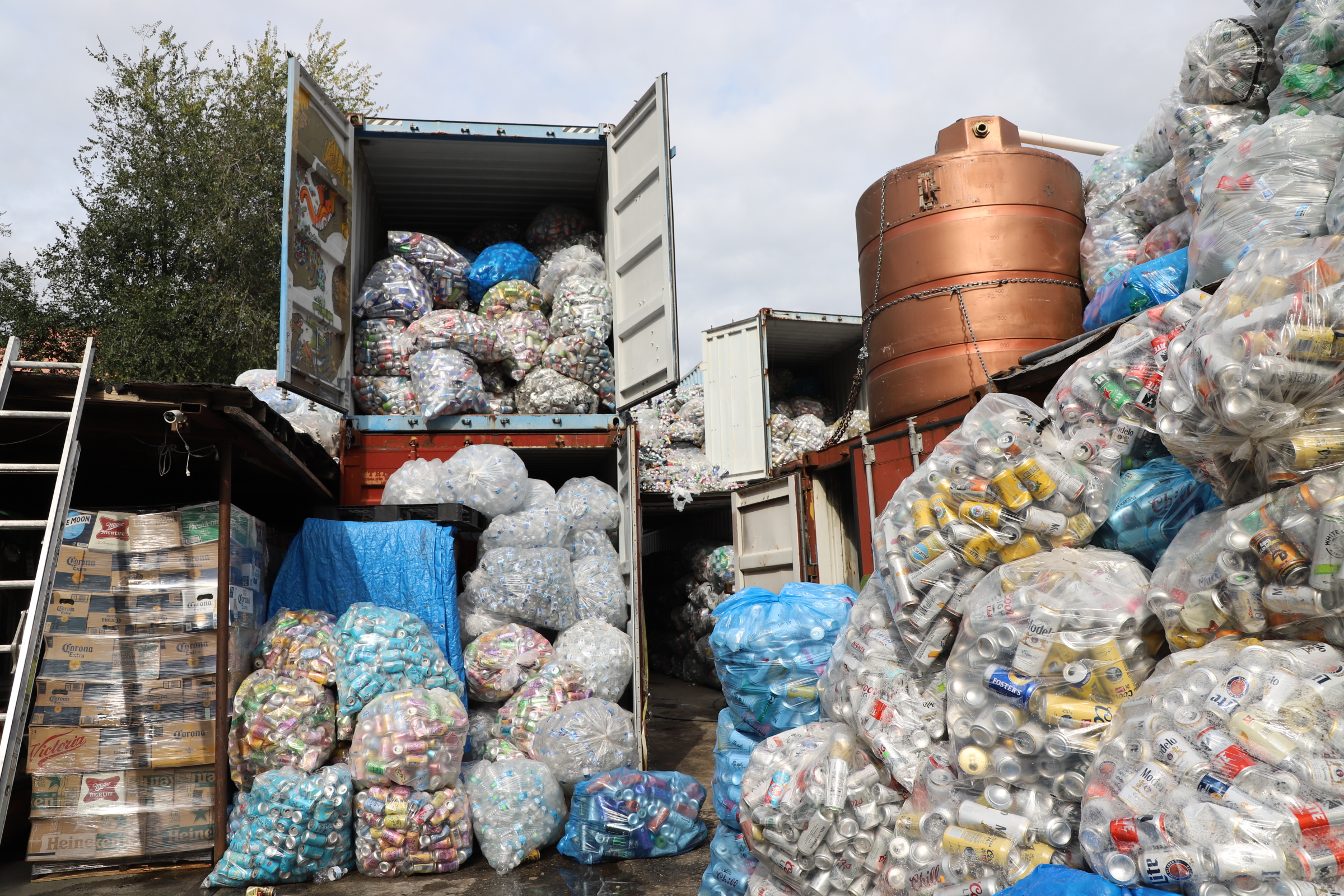 stacked open shipping containers stocked full of bags of aluminum cans