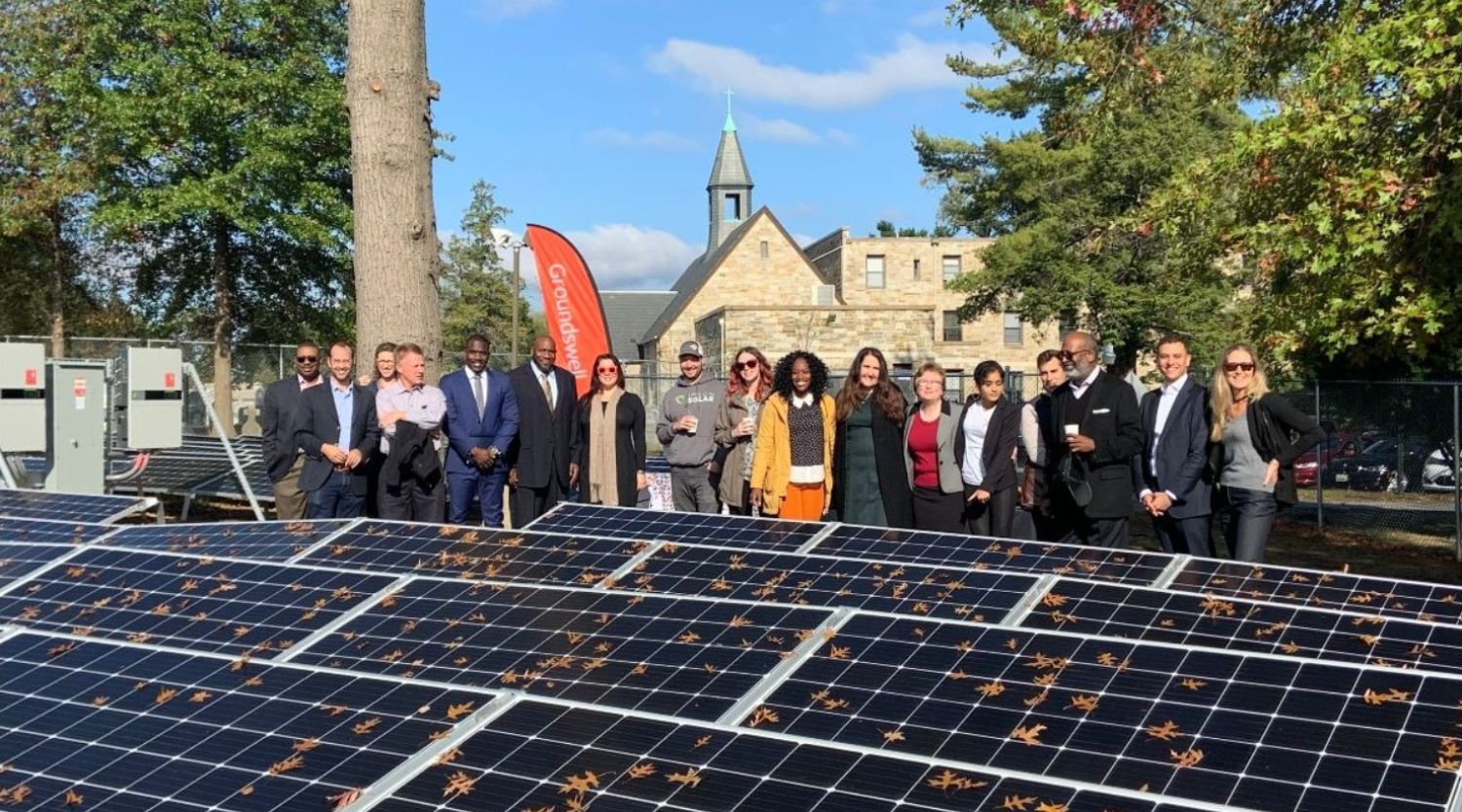 A group of people pose for a photo in front of a solar panel array. A group of people pose for a photo in front of a solar panel array.