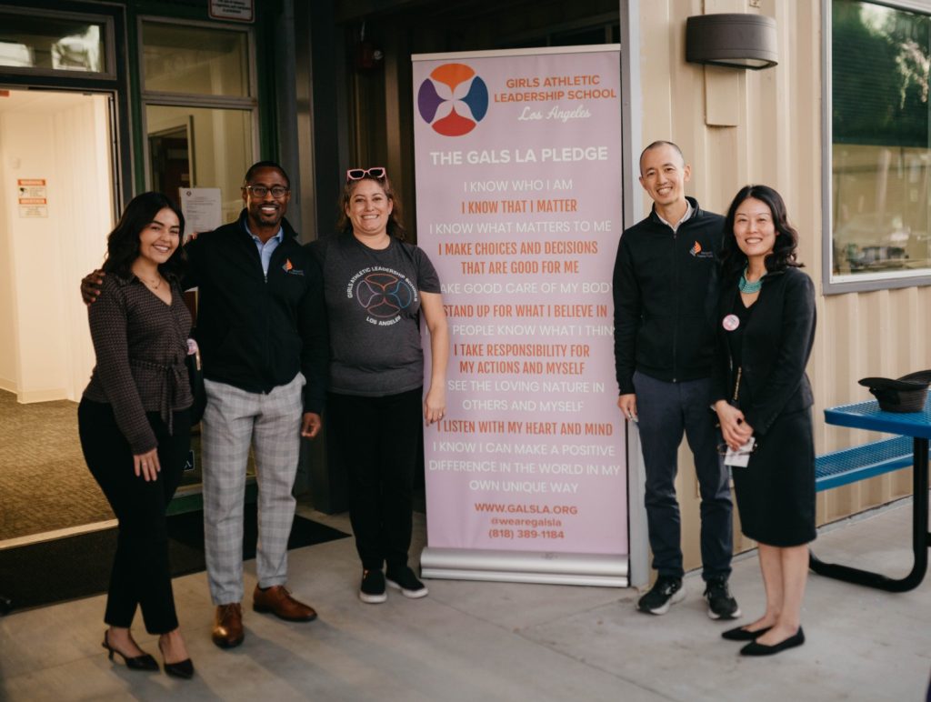 A group of people smiling in front of a sign at a ribbon cutting ceremony.